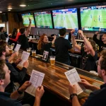 Betting excitement at a sports bar as patrons use sbobet app to wager on live games amid a vibrant atmosphere.